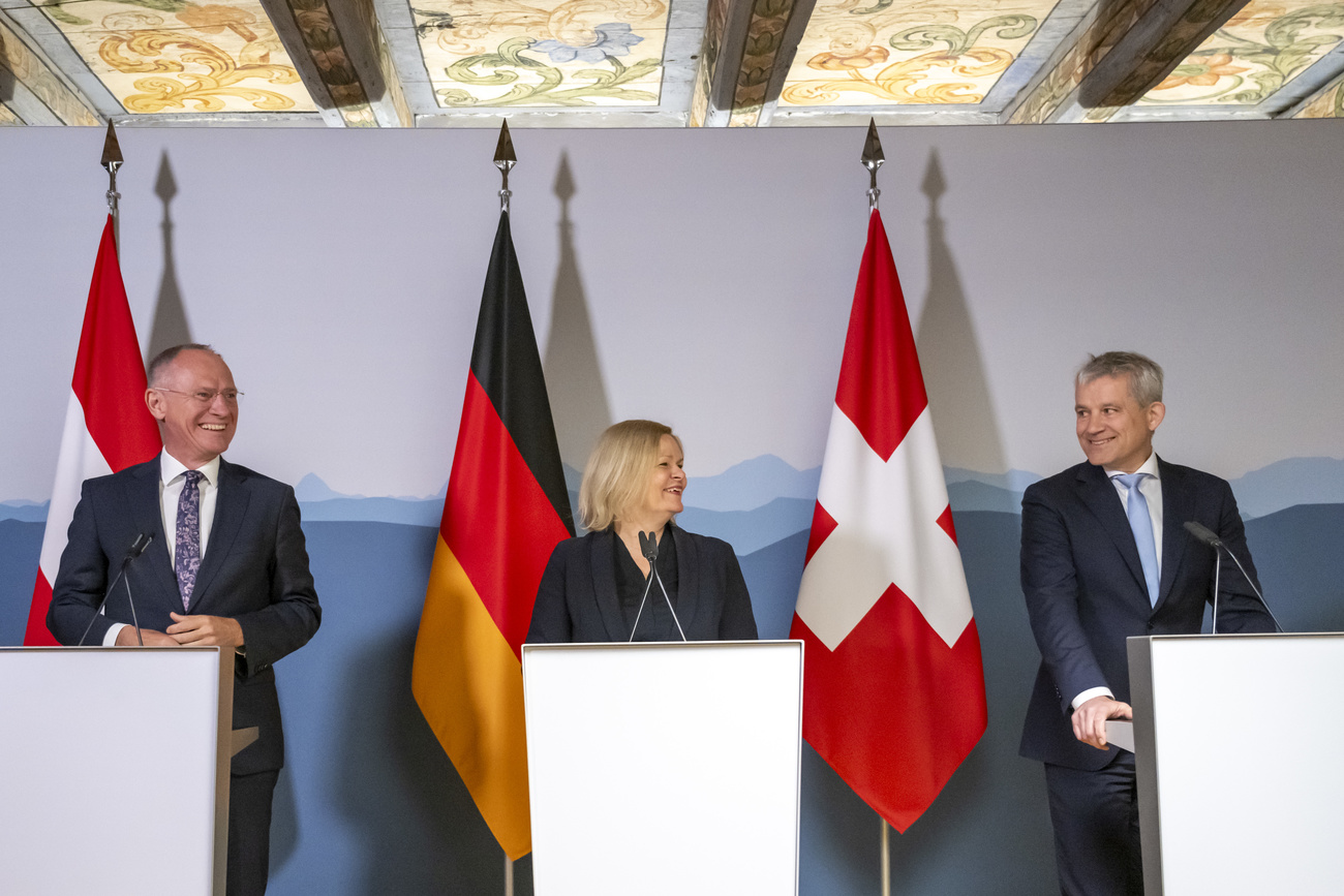 From left, Gerhard Karner, Nancy Faeser and Beat Jans, interior ministers of Austria, Germany and Switzerland, stand behind podiums and in front of their respective flags at a media conference. They are smiling and speaking together.