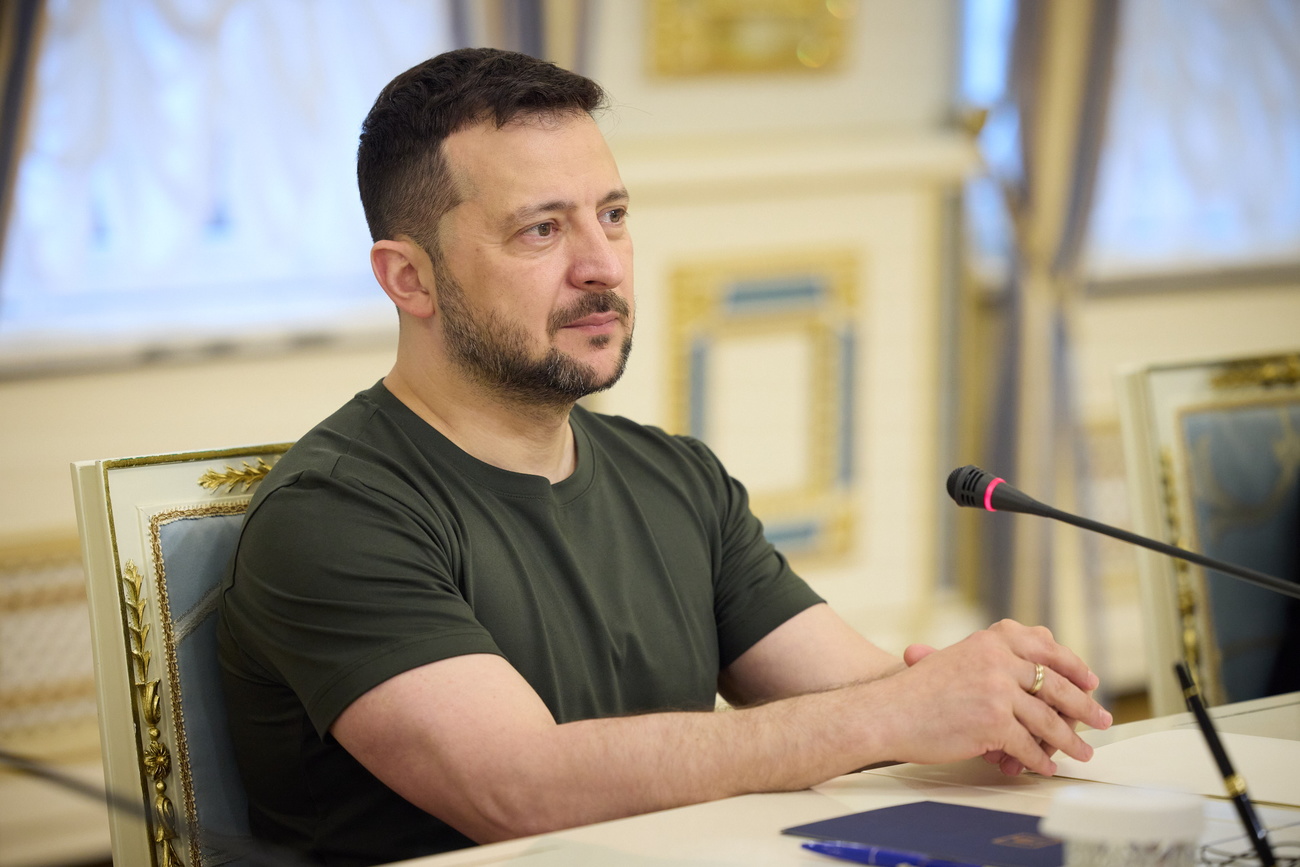 The Ukrainian president Vladimir Zelensky, seated at a table before a microphone.