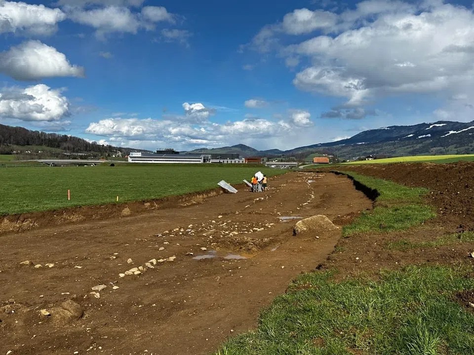 Grüne Wiese mit brauner ausgegrabener alten Römerstrasse