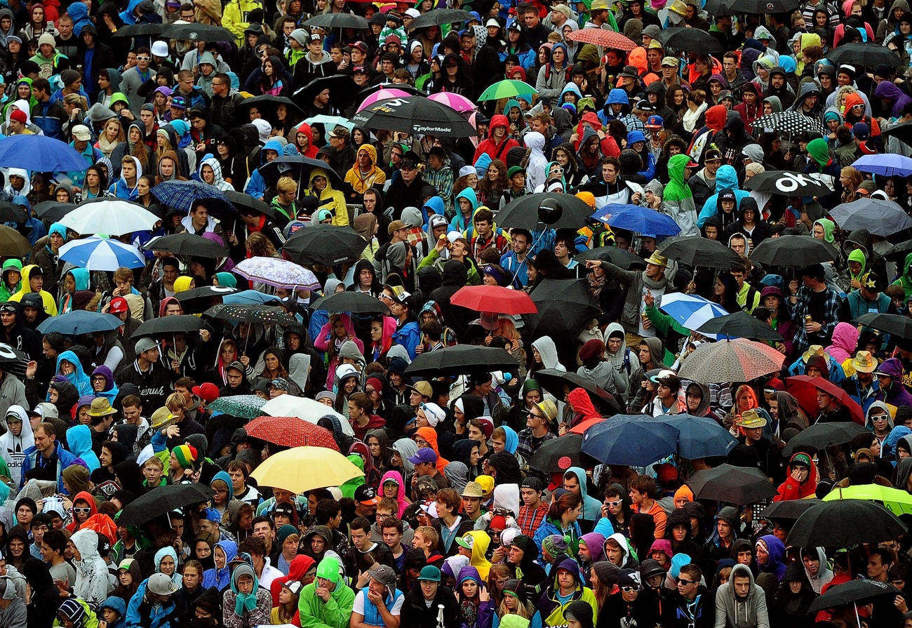 A crowd of people, some holding umbrellas of different colours.
