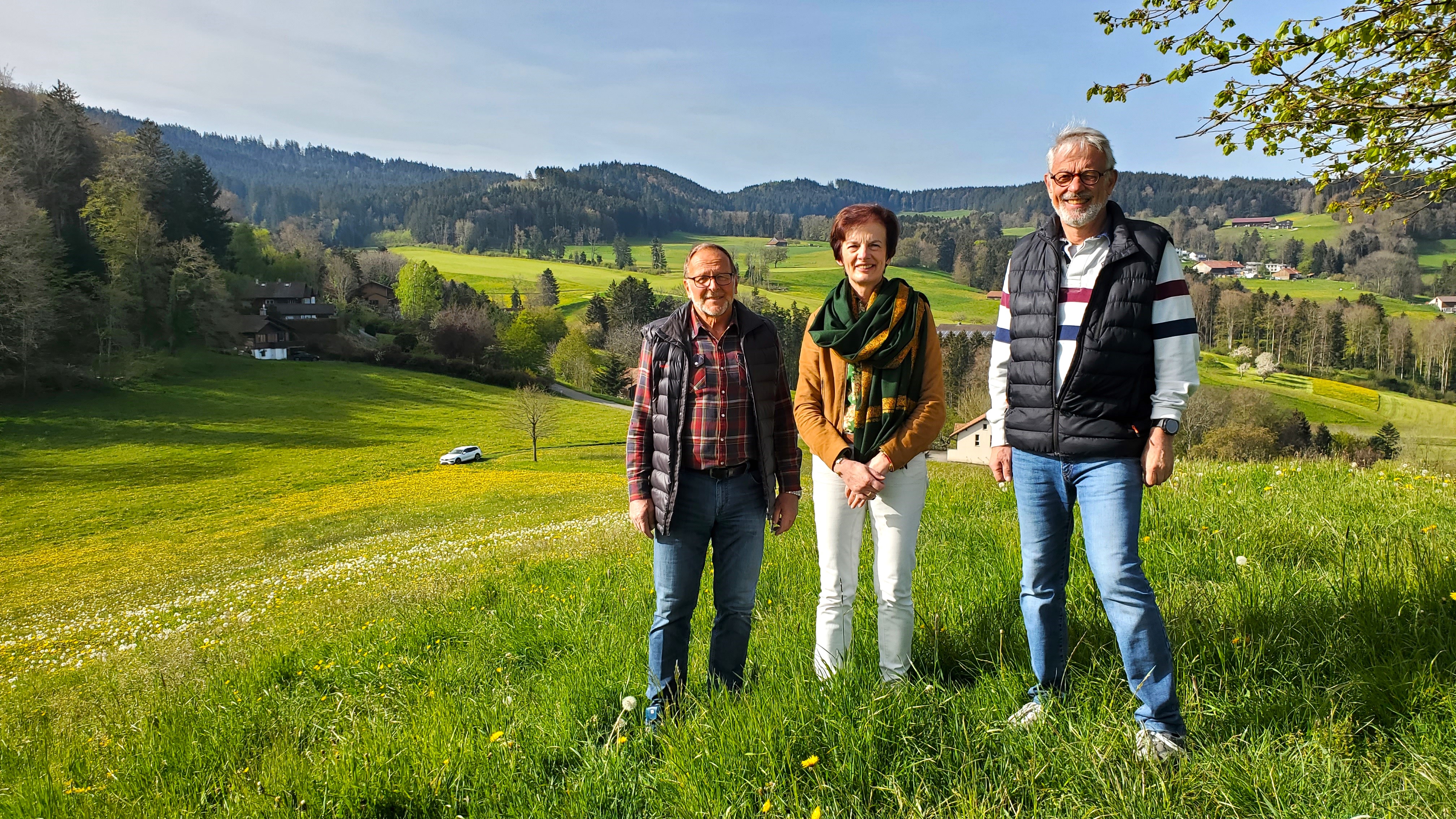 tre persone su un prato fiorito e alle loro spalle delle foreste
