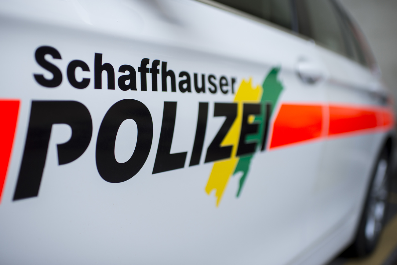 The Schaffhausen Police logo on the side of a white police car: it says ‘Schaffhauser Polizei’ or ‘Schaffhausen Police’ in big black letters with a neon orangey red line running through it and two diagonal stripes in yellow and green