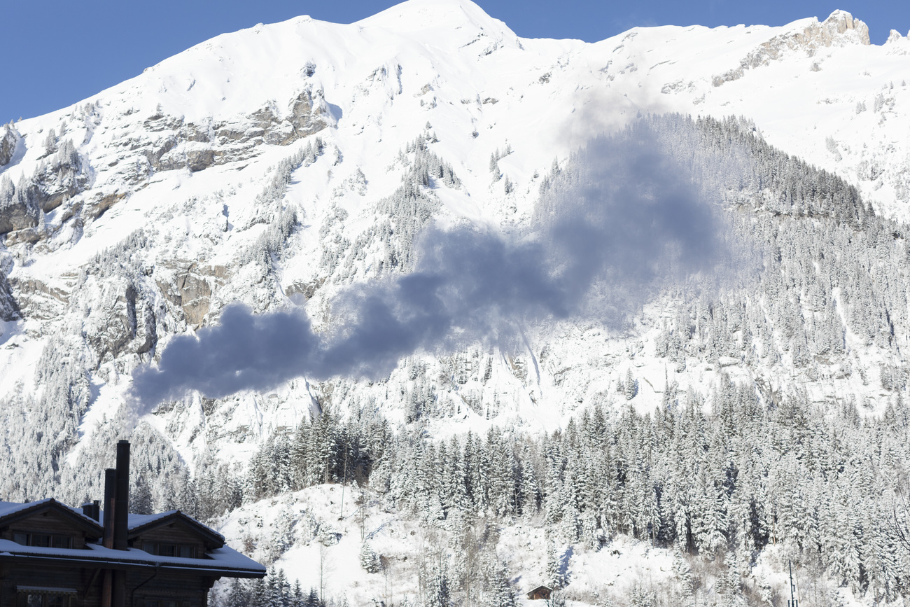 Smoke rises from a chimney in front of a wall of snow-covered mountain.