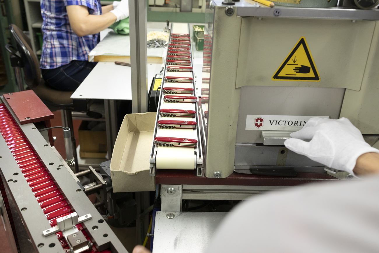 Arbeiter in der Victorinox-Fabrik überwachen die Produktion von Taschenmessern der Schweizer Armee, während Maschinen und Förderbänder arbeiten
