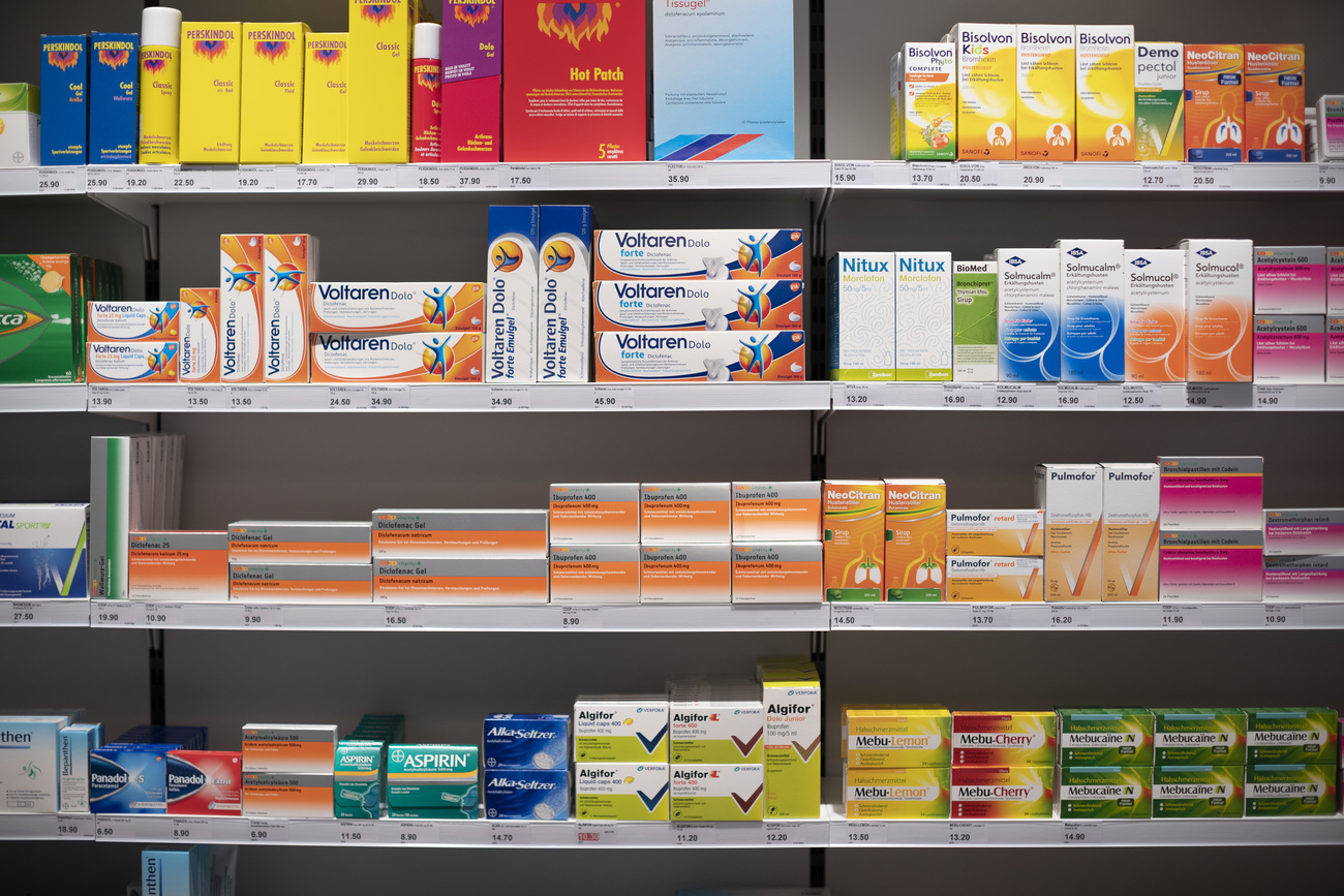 Various medications are shown stacked on shelves in a pharmacy.