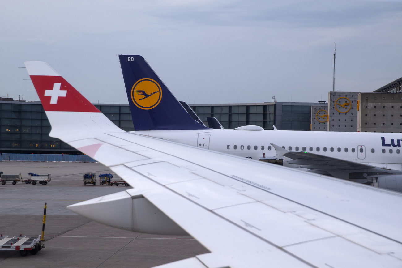 The tail and logo of a Lufthansa aircraft parked on the tarmac of Frankfurt Aeroport is pictured from a window of an aircraft Airbus A220-300 of the Swiss International Air Lines, with the swiss logo in view, in Frankfurt, Germany, Friday, June 4, 2021.