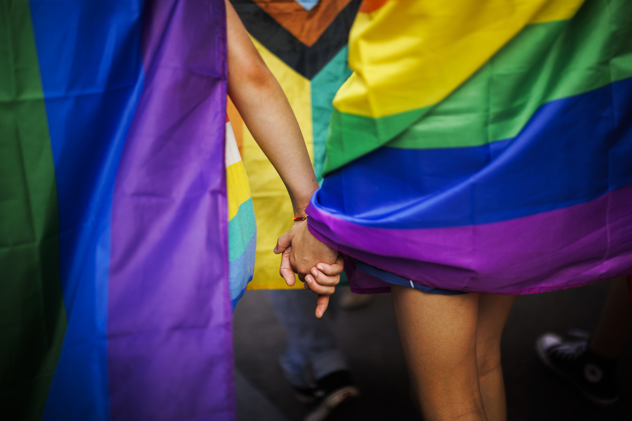 Zwei Frauen, die Pride Flaggen tragen, halten sich die Hand.