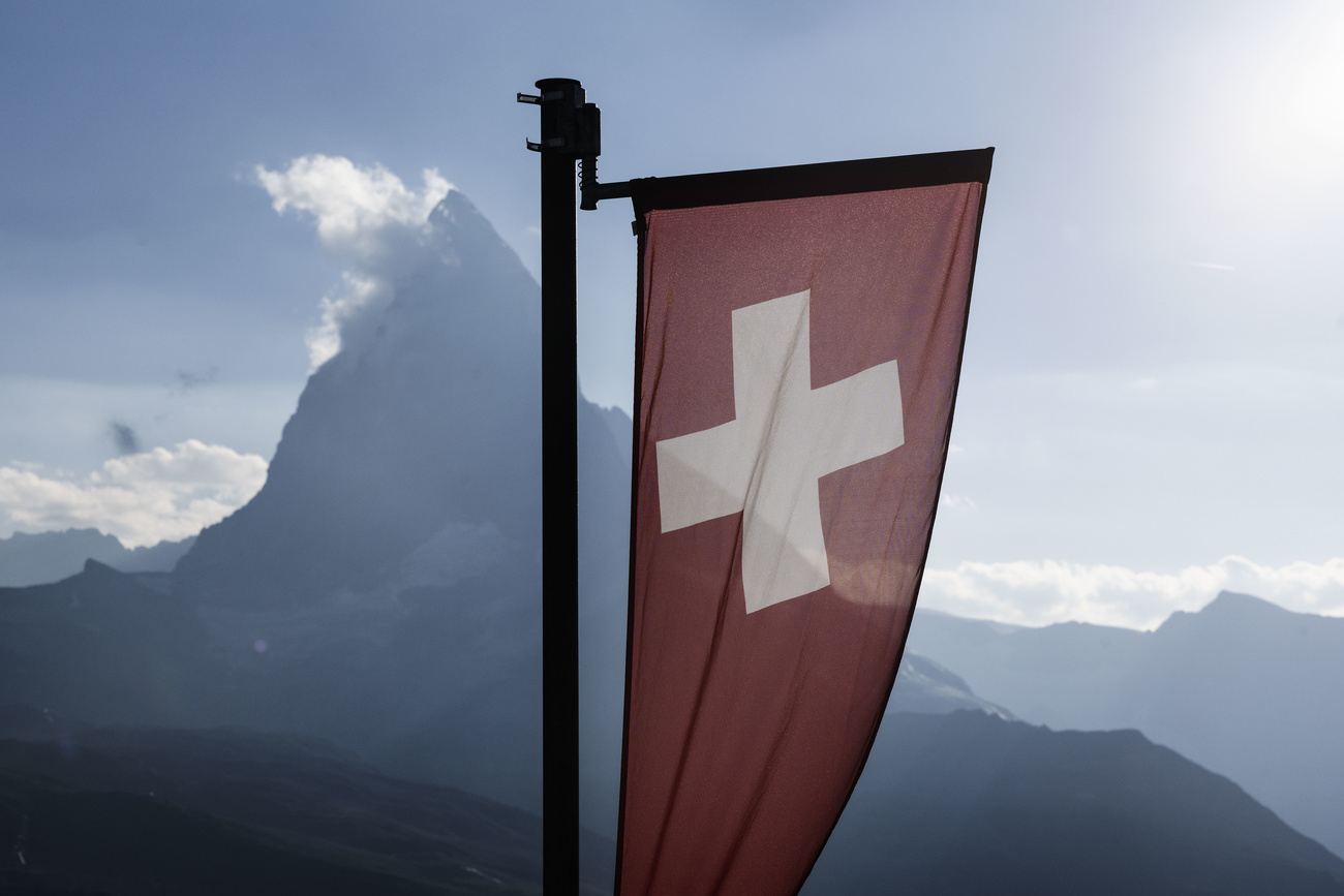 A Swiss flag is in the foreground in front of the recognisable ‘pyramid’ shape of the Matterhorn.