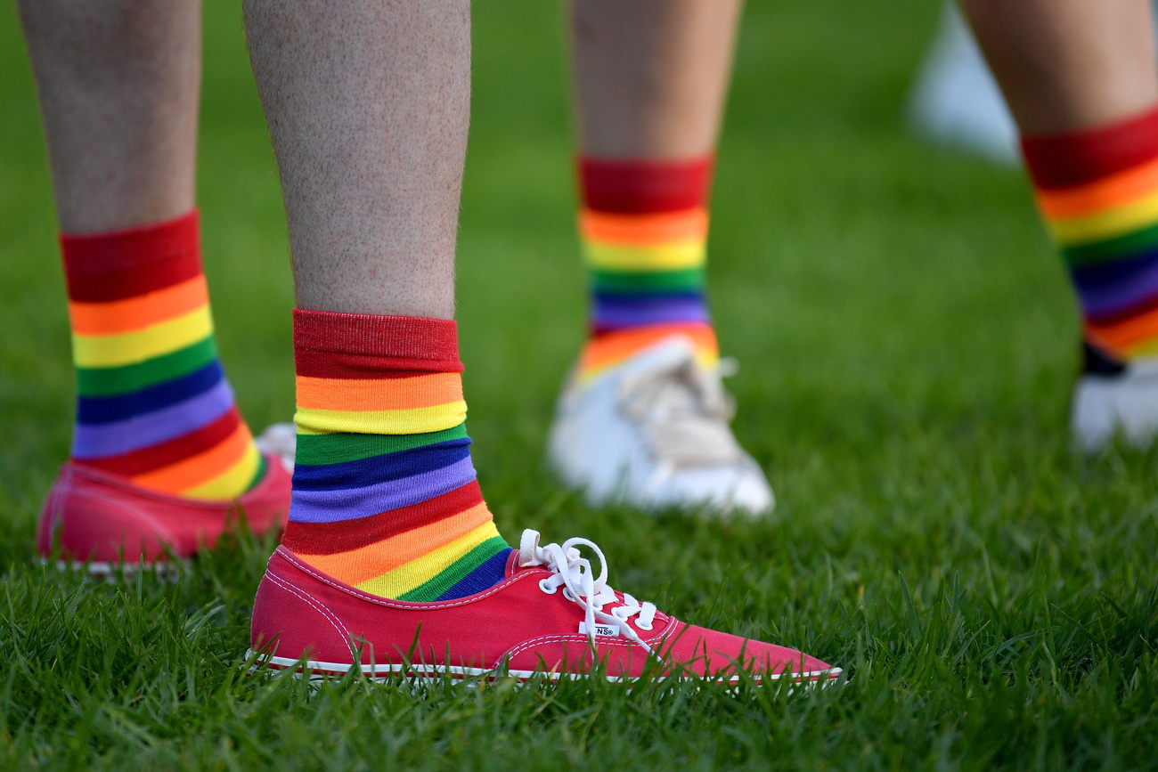 Two pairs of feet are shown, clad in sneakers and rainbow socks.