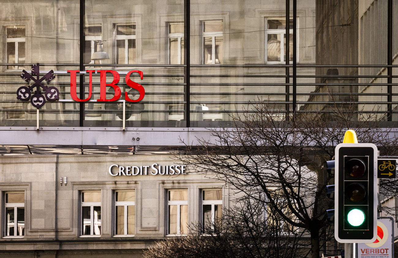 The Credit Suisse bank logo is shown on a building, overtop is a larger UBS logo. A green traffic light is in the foreground.
