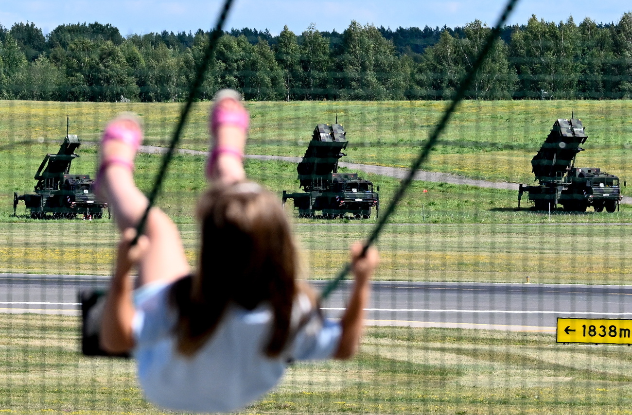A picture of a young child on a swing with some missile defence systems in the background.