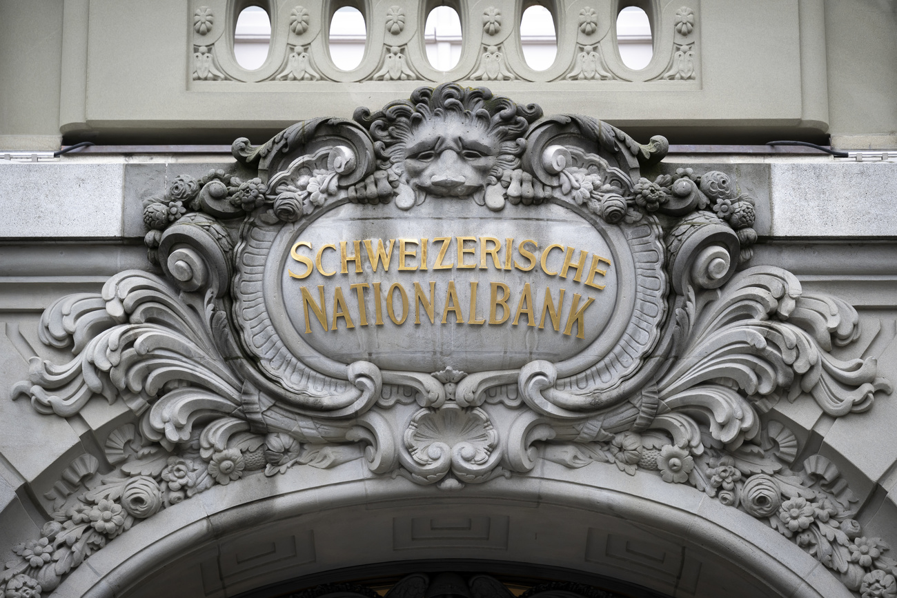 The facade of the Swiss National Bank including a decorative grey stone border around 'Swiss National Bank' in gold lettering, with flourishes, floral shapes and a lion's head at the top