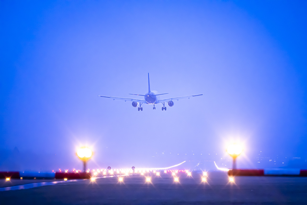An airplane descends to land on a lit-up runway.