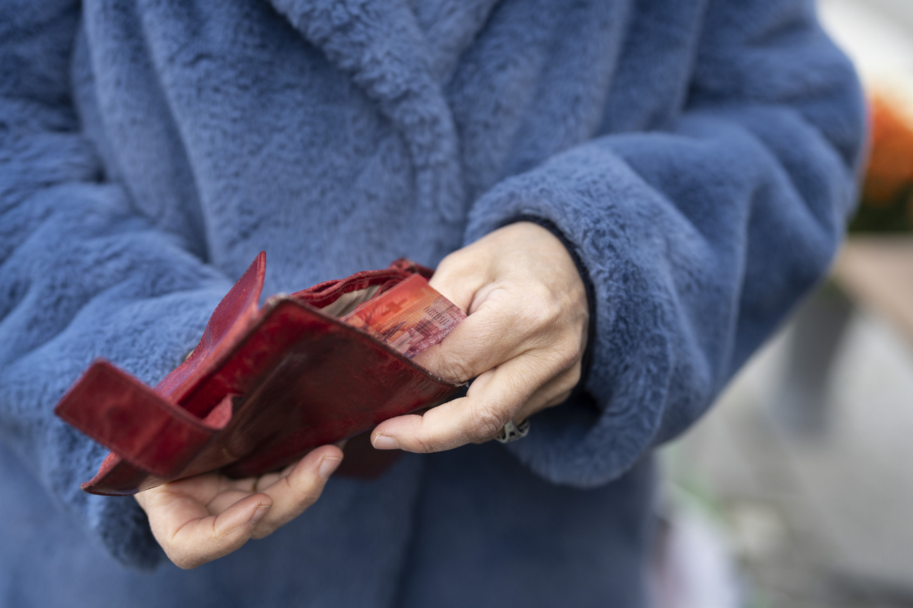 The hands of a woman wearing a fluffy light blue coat reach into a dark red wallet and pull out some bank notes