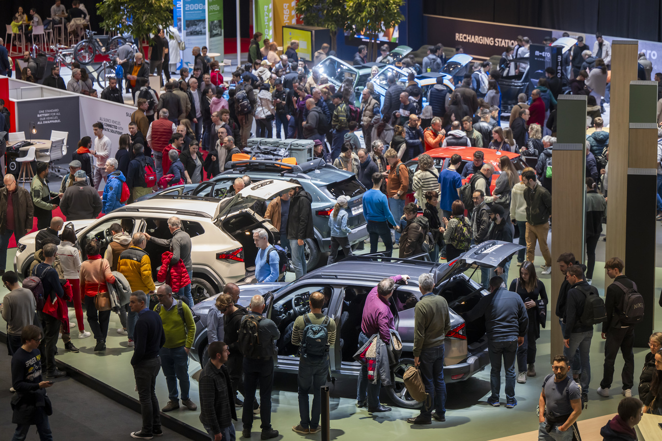 A crowd of people is shown standing around various cars on display at a motor show.
