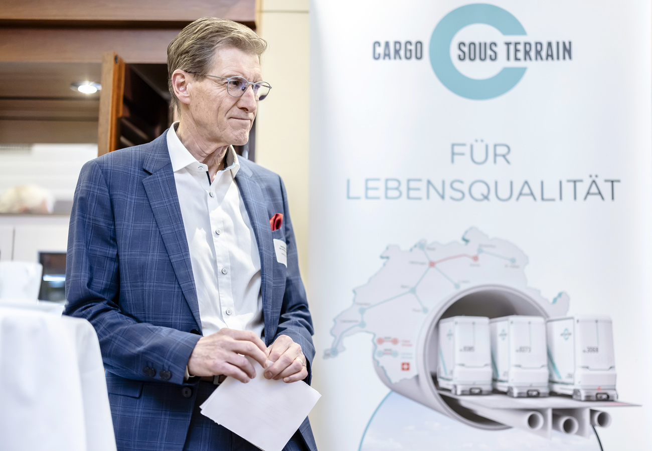 The CEO of Cargo sous terrain stands in front of one of his company's posters.