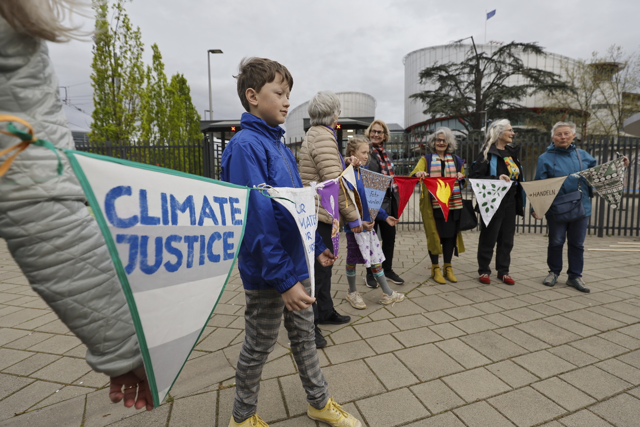 activists including a boy hold flags in front of the European court, waiting for their decision on a cloudy day in April 2024