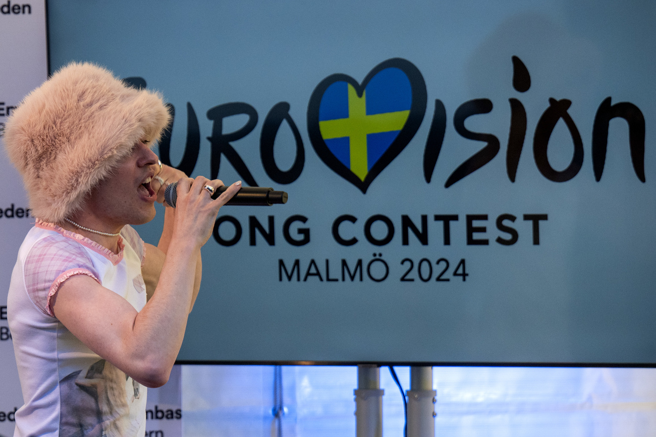 The singer Nemo is shown performing in front of a poster for the Eurovision Song Contest