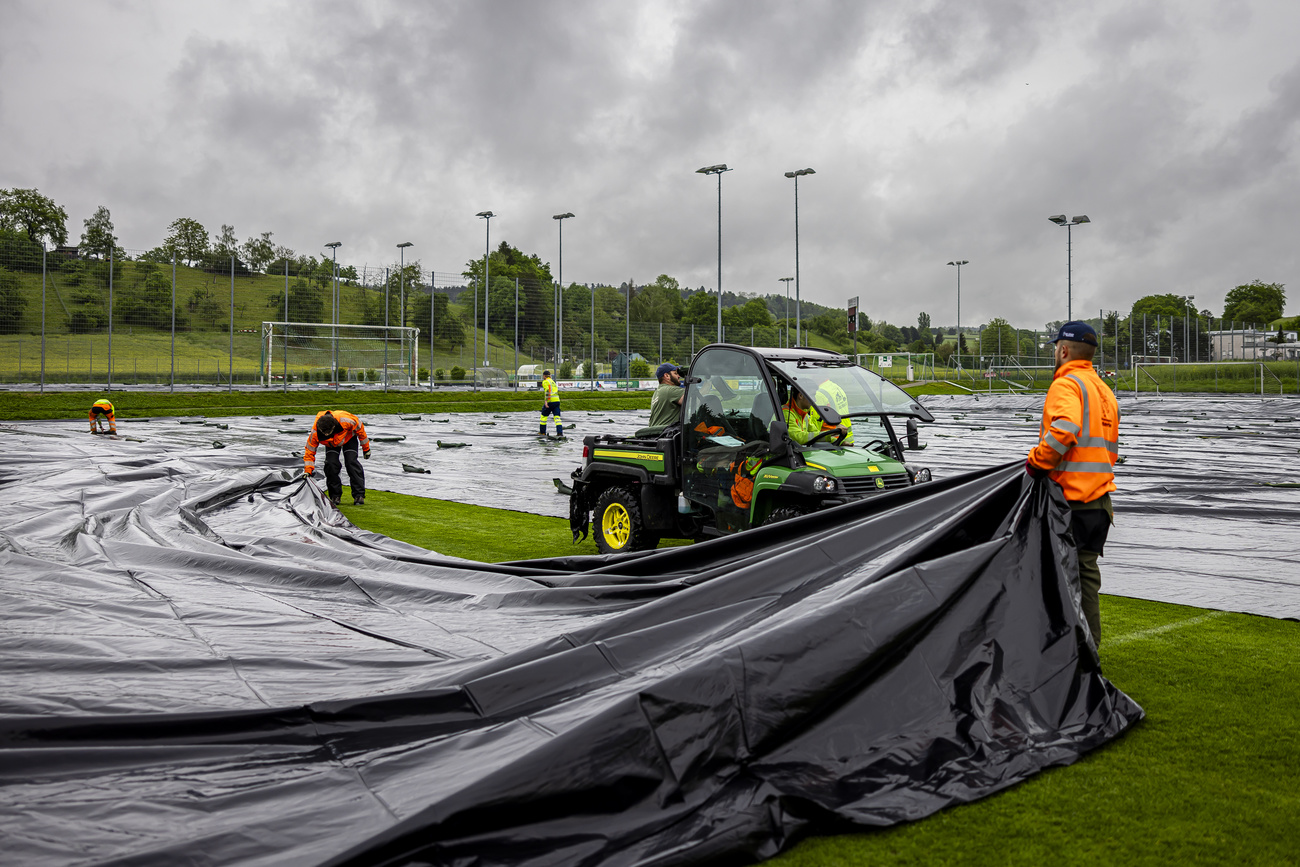Personnel installant des bâche en plastique sur un terrain de football