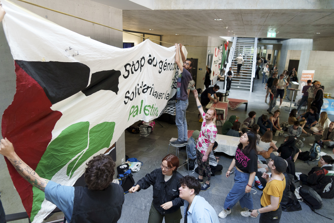 Students hang up large signs and sit on the floor in a university building in Fribourg