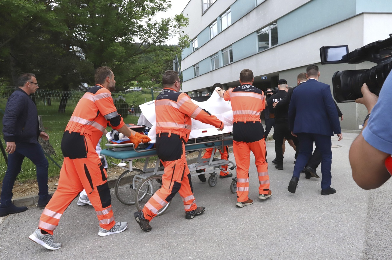 Rescue workers in orange uniforms wheel Slovakian Prime Minister Robert Fico, covered by a white sheet, into a hospital building on a stretcher.
