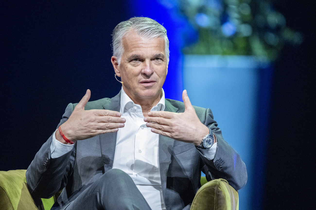 A man (UBS CEO Sergio Ermotti) is shown seated and gesturing with his hands.