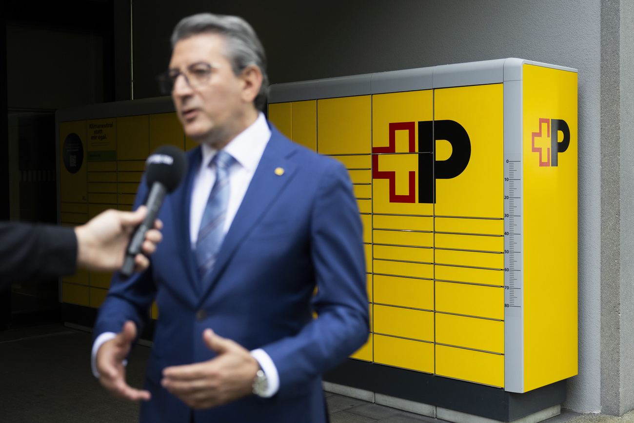 Roberto Cirillo, CEO of Swiss Post, speaks during an interview with yellow post boxes in focus in the background with the Swiss Post logo