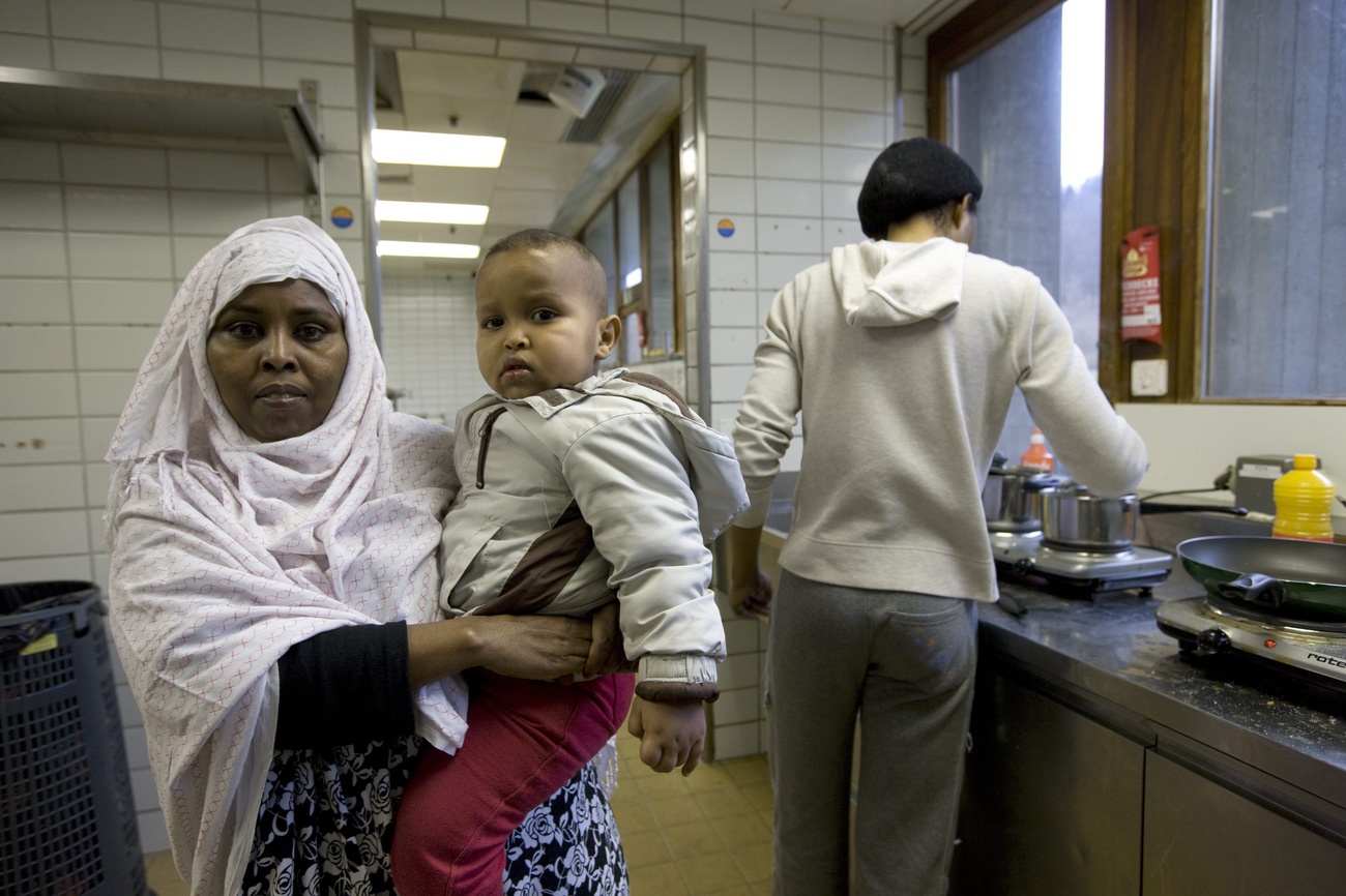 Picture of a woman holding a baby and a man cooking in the background