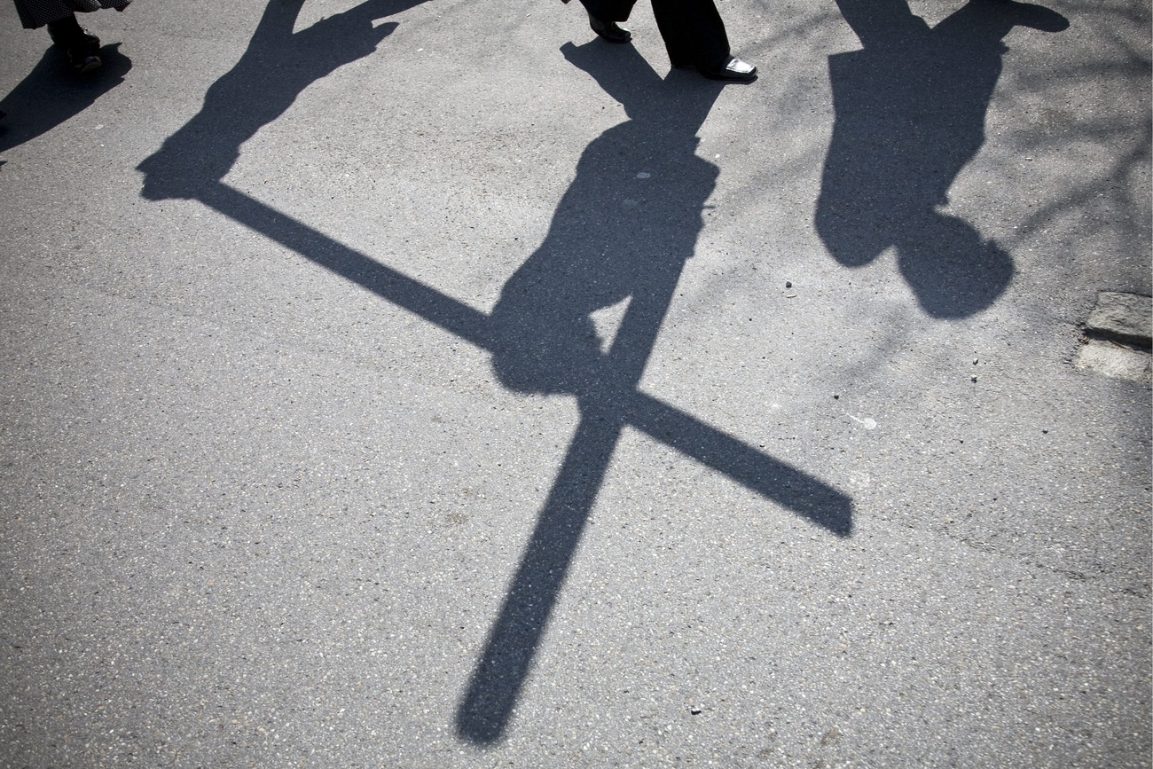 shadows of people on the ground, two of whom are carrying a large cross