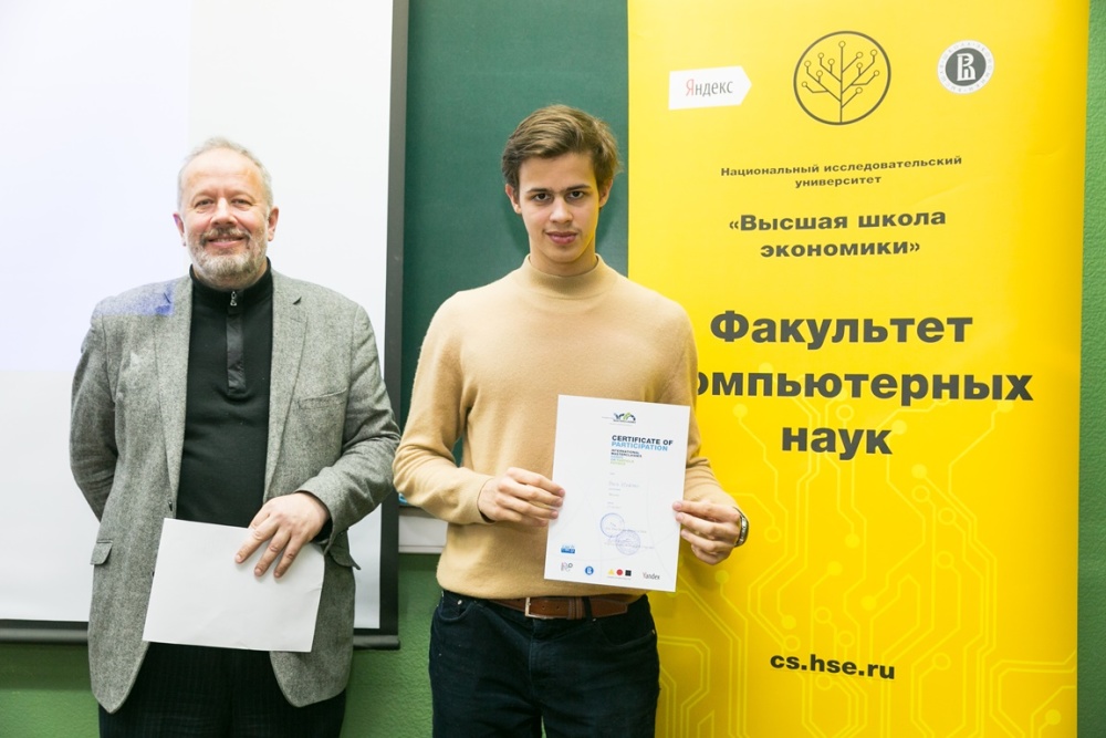 Un professeur et un étudiant prenant la pose devant une affiche