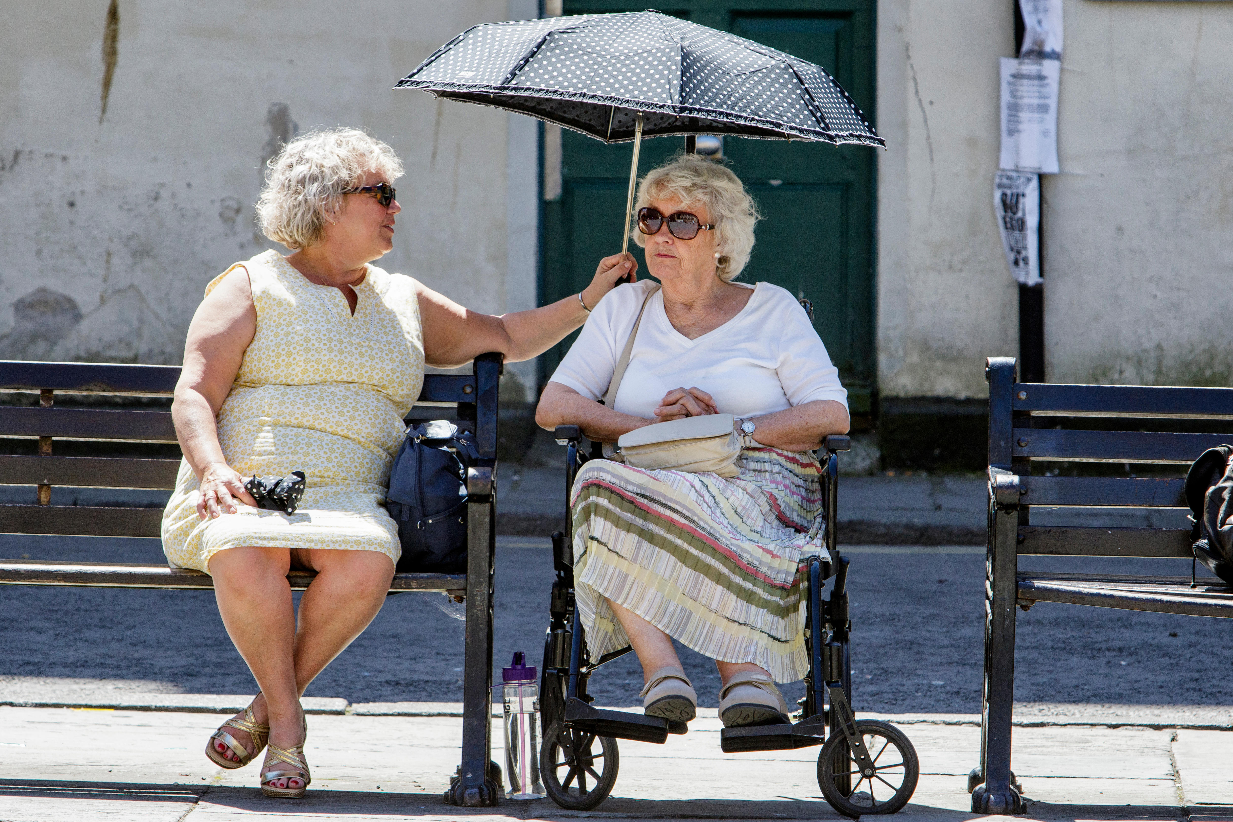 Zwei alte Frauen, von denen eine einen Regenschirm über die andere Hält, zum Sonnenschutz.