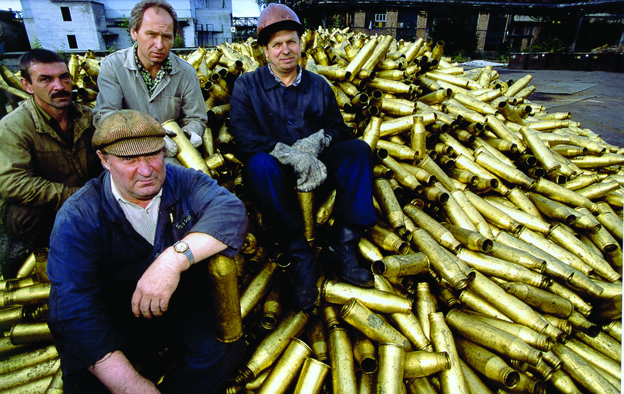 men sitting on pile of brass weapon casings