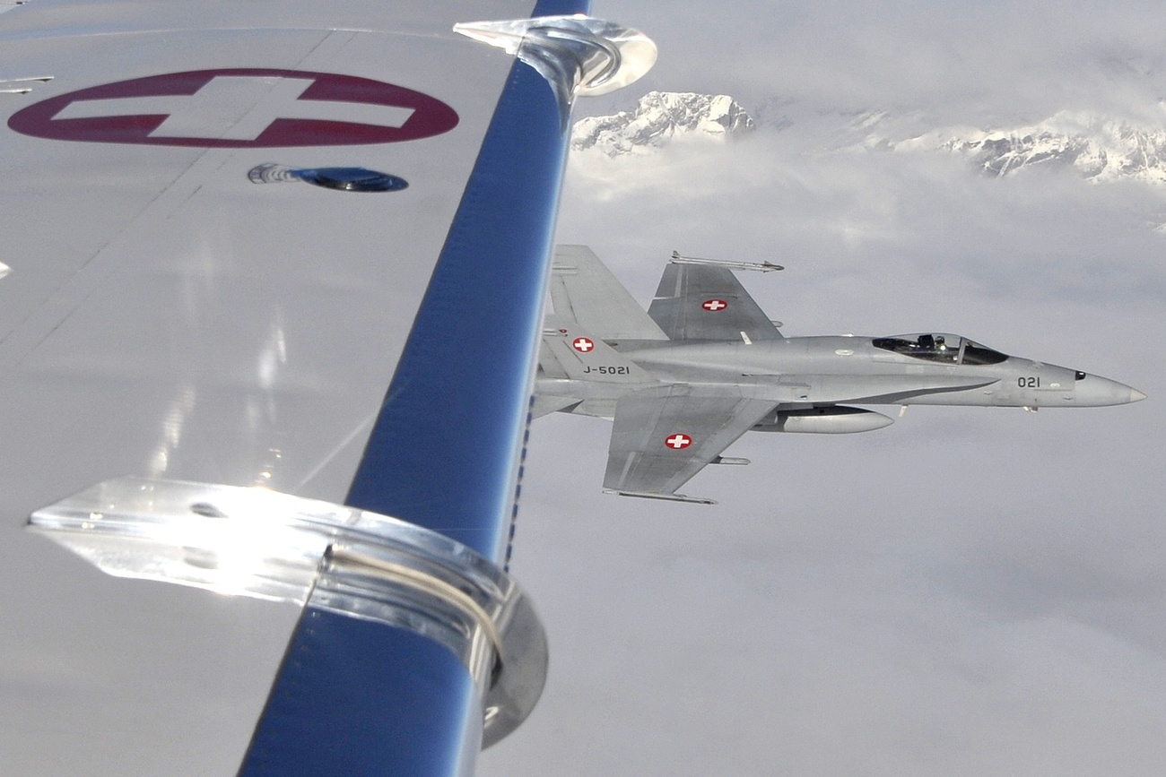 A FA18 Hornet from the Swiss Army flies next to a civil plane during an exercise. The civil plane's wing is visible with a Swiss cross.
