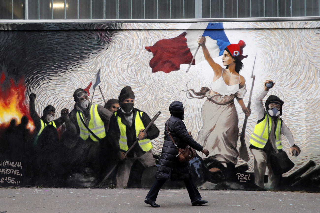 una donna cammina davanti a un murales che raffigura la protesta dei gilet gialli