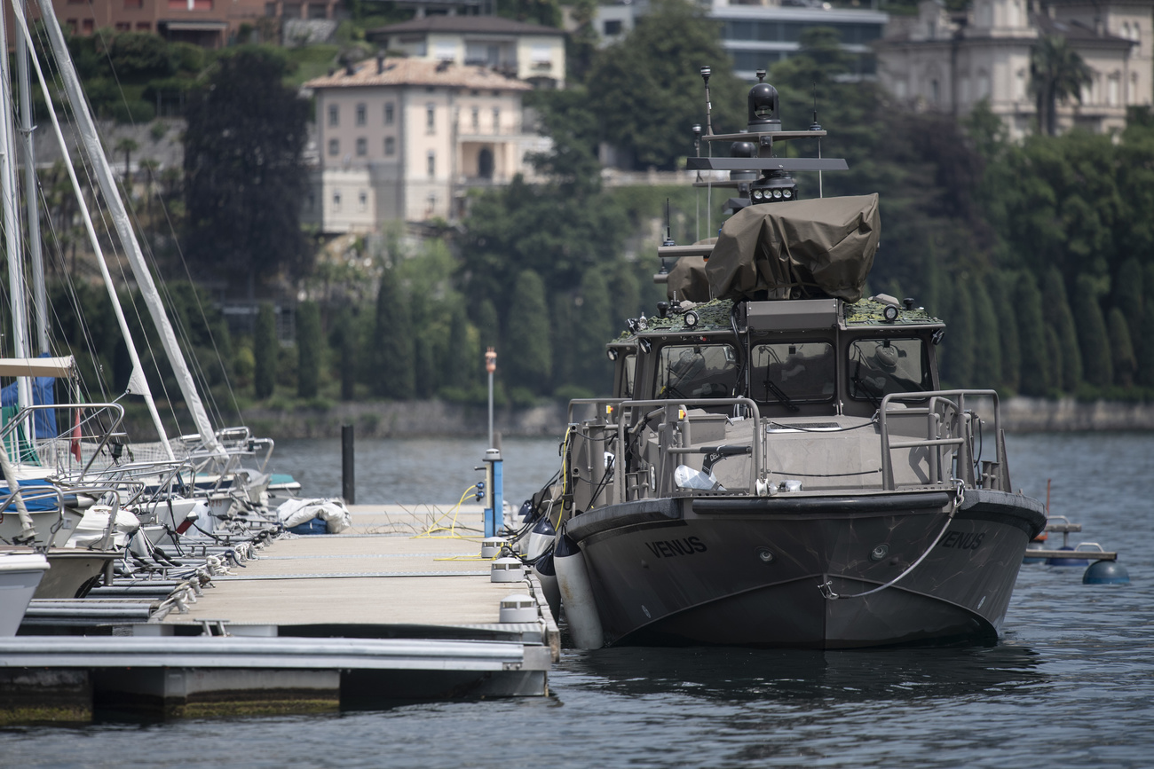 A military boat is docked to a pier with civilian sailboats on the other side.