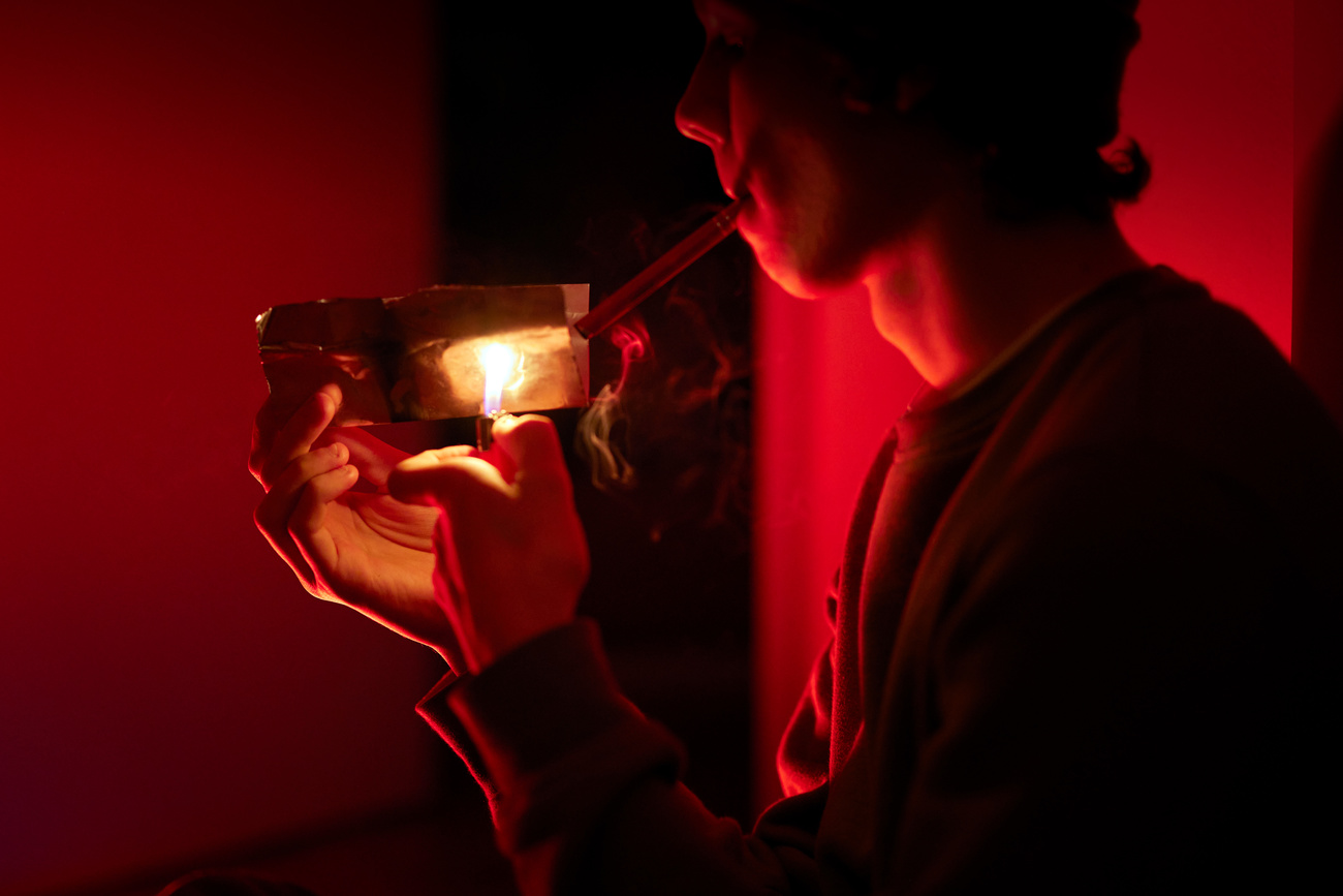A teenage male is shown in profile, smoking crack in a dim environment.
