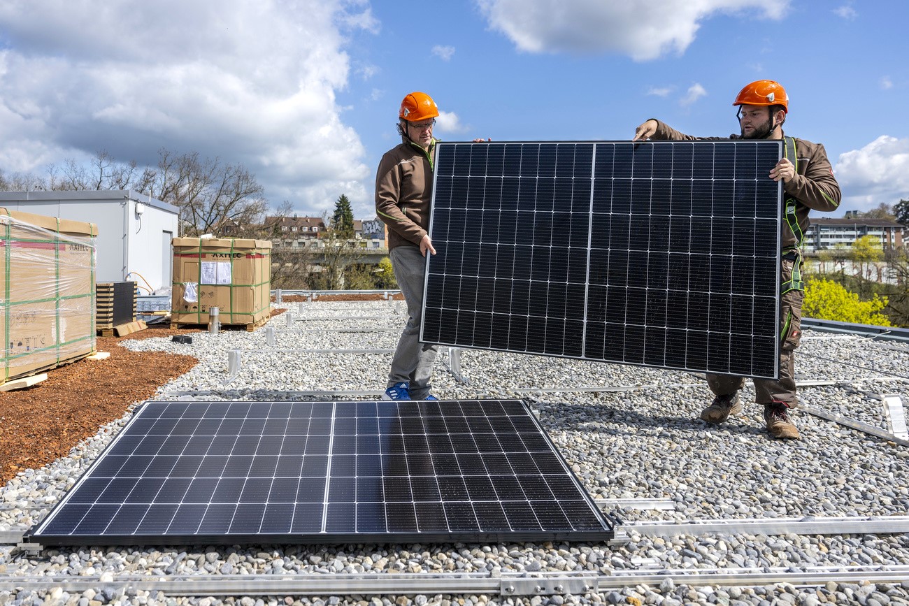 Zwei Männer auf einem Dach mit einem Solarpanel in der Hand.