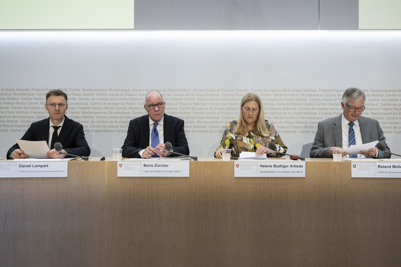 Four officials sit behind a desk with their name cards and microphones at a press conference
