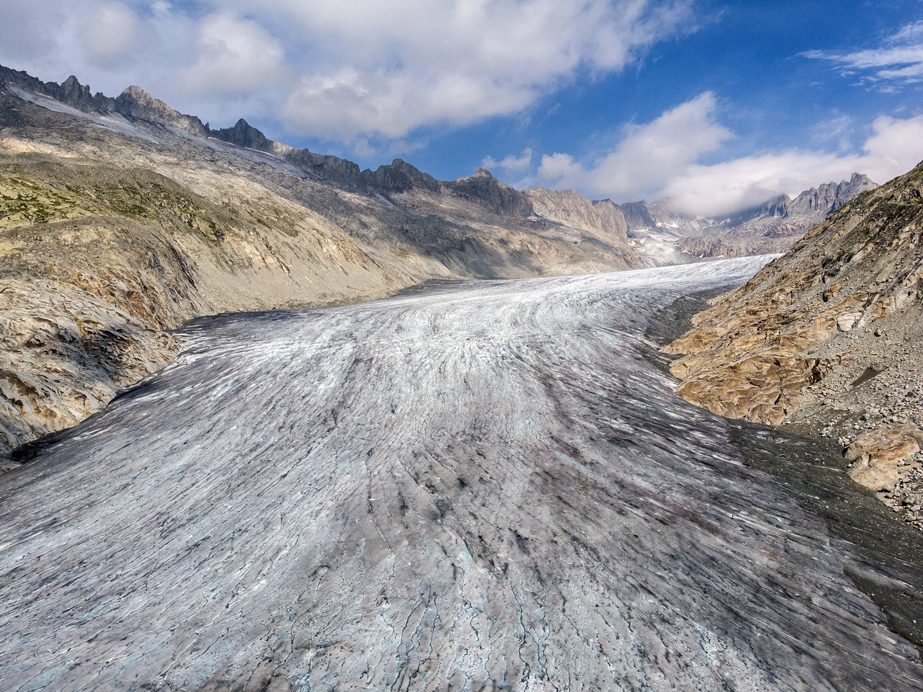 The Rhone glacier, flanked by brown mountains on either side.