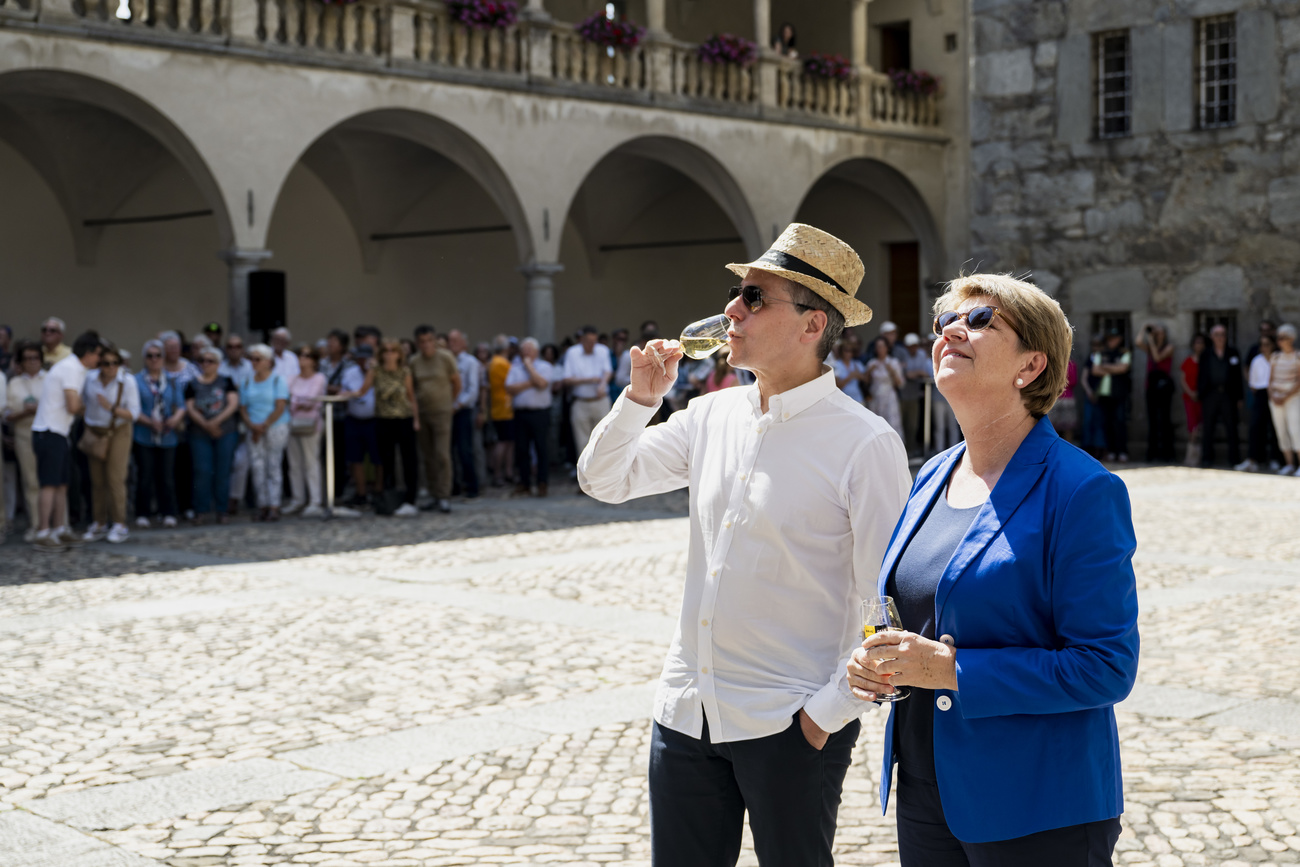 Two members of the Swiss federal goverment, Amherd and Cassis, are shown standing in the sun next to a castle.