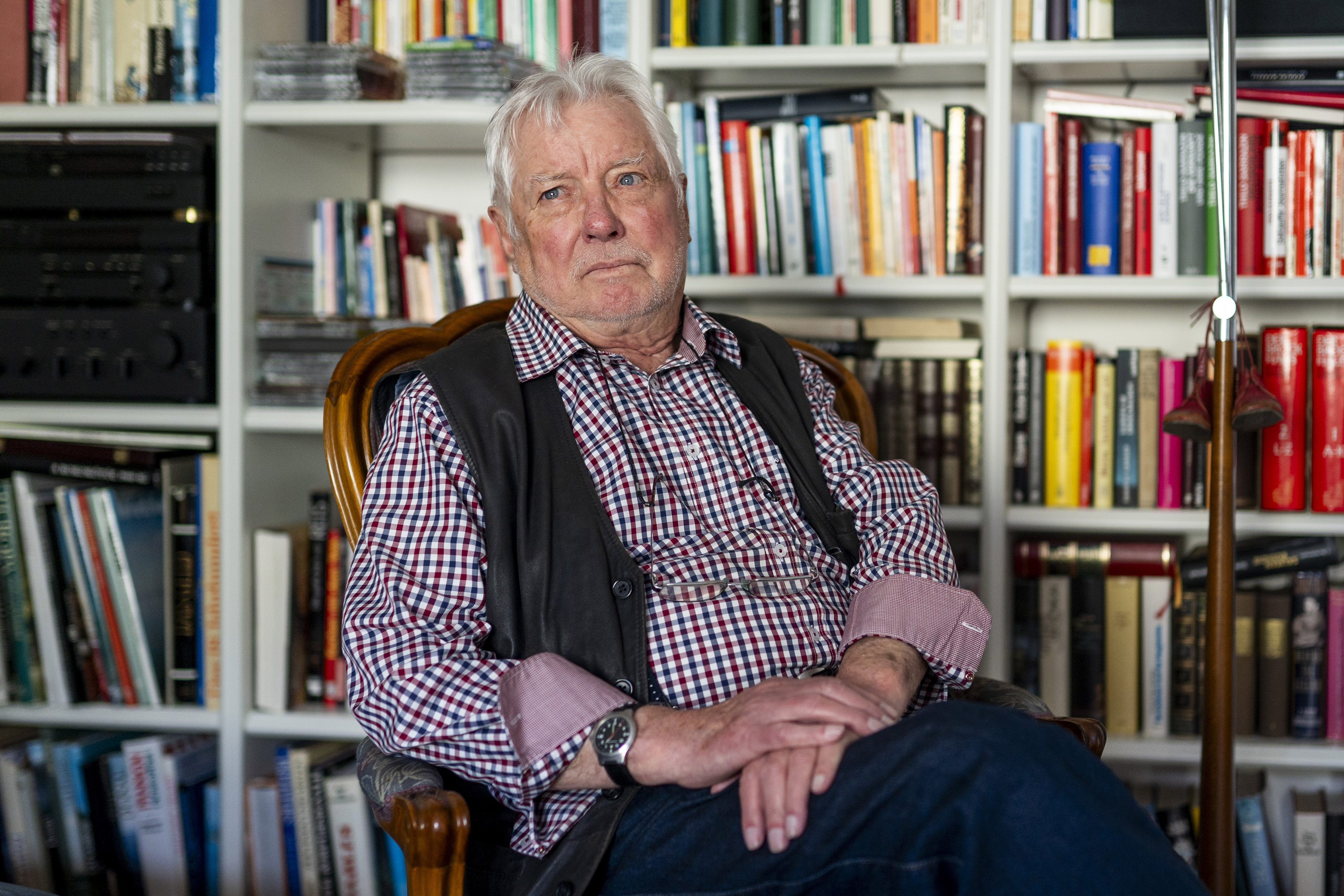 Um idoso sentado na frente de uma estante cheia de livros