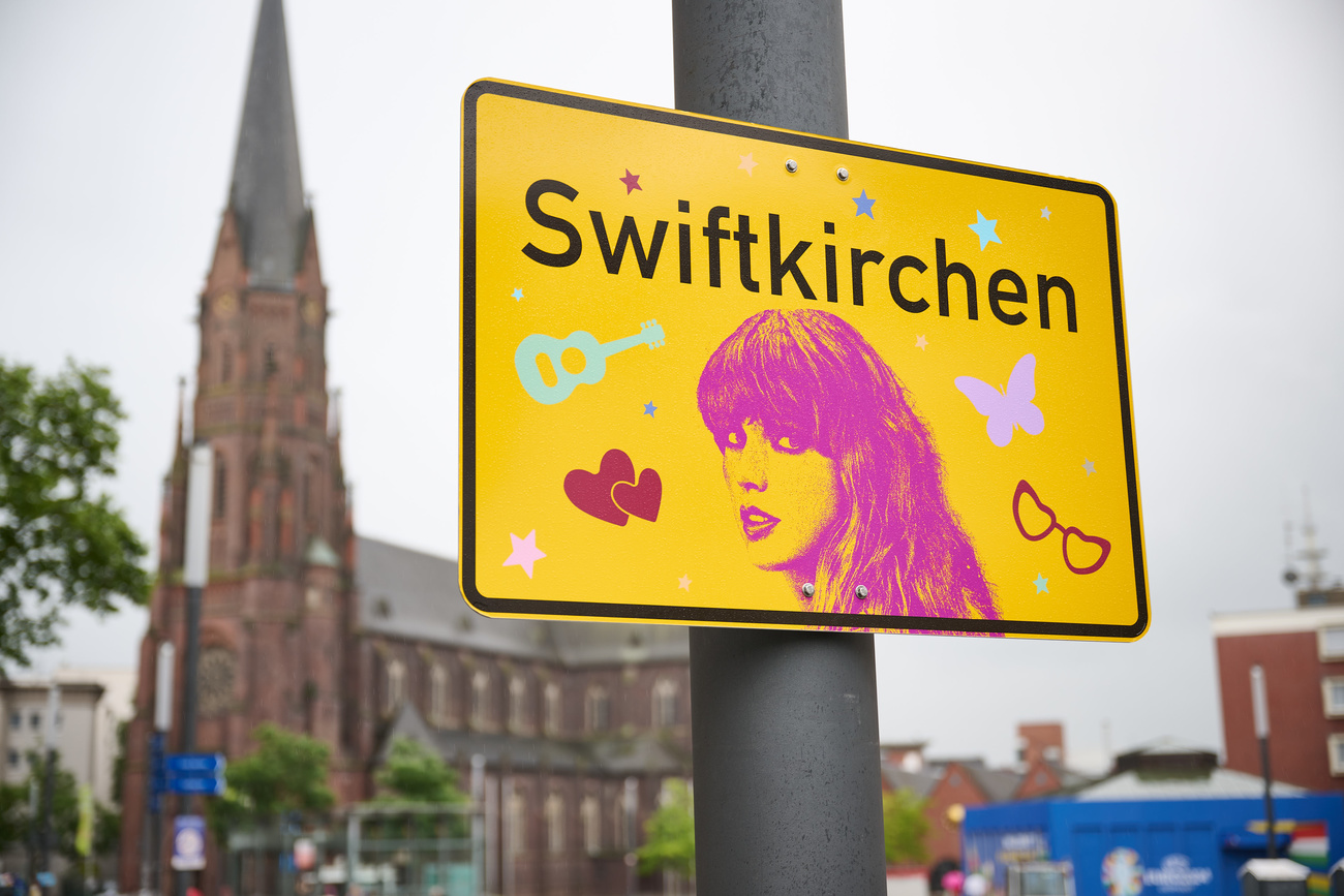 North Rhine-Westphalia, Gelsenkirchen: The "Swiftkirchen" town sign in honour of musician Taylor Swift hangs on Heinrich-König-Platz, in front of the St. Augustinus provost church. Music superstar Taylor Swift will be coming to Gelsenkirchen for concerts in mid-July. In a petition, Aleshanee suggested renaming the town "Swiftkirchen" during the singer's stay. More signs are to be put up around the town.