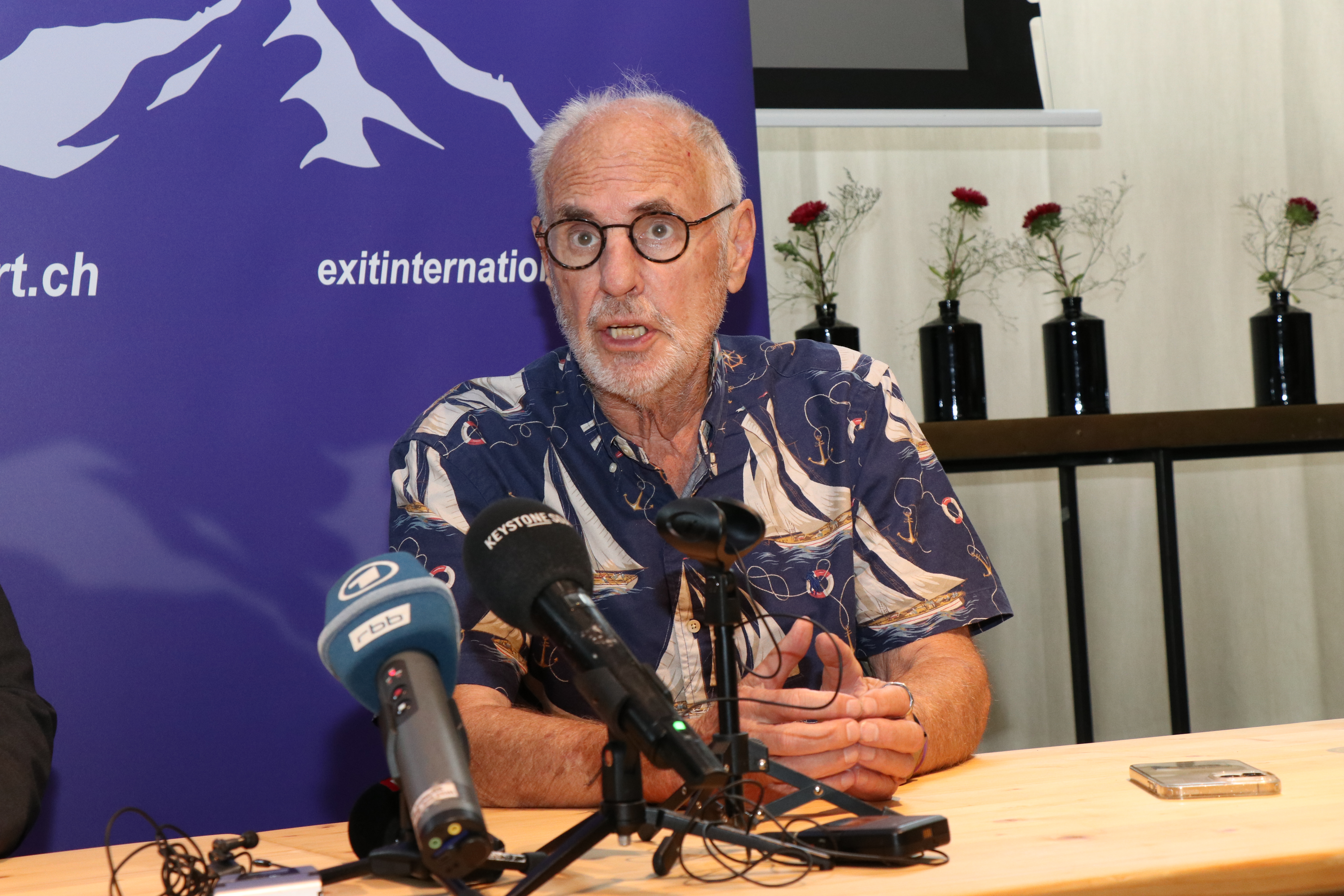 Un homme assis devant des micros lors d'une conférence de presse.