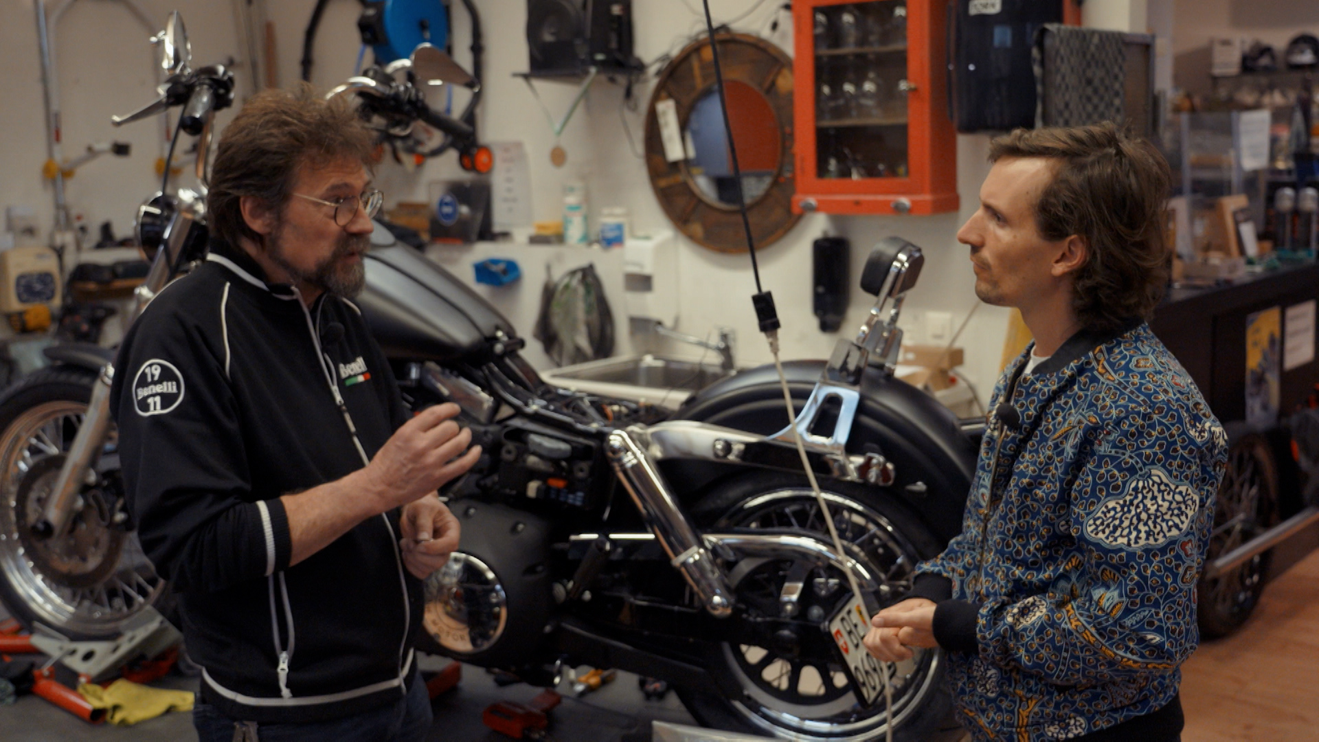 two men talk in a motorbike workshop