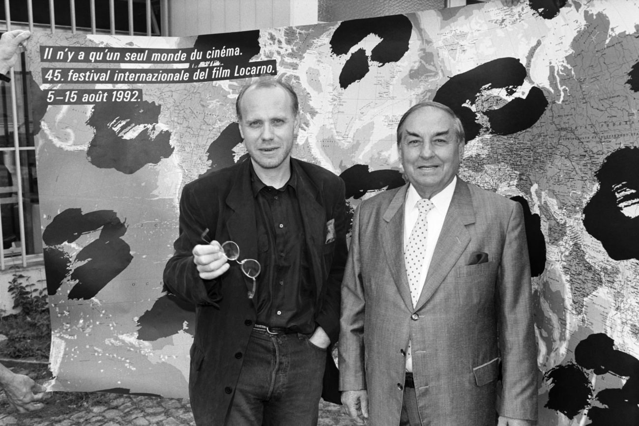 due uomini in piedi davanti al manifesto del festival del film di locarno in una foto in bianco e nero