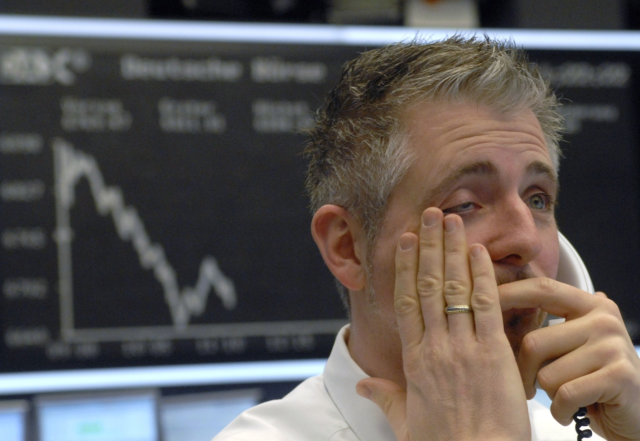 Ein zerknirscht aussehender Börsenmakler telefoniert vor einem tief negativen Chart auf einer Anzeigetafel.