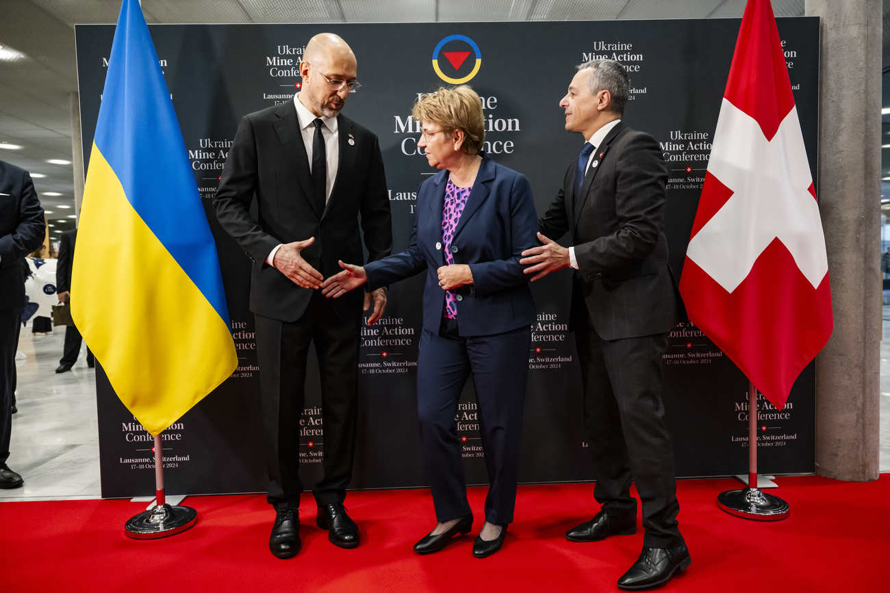 Denys Shmyhal, left, Prime Minister of Ukraines and Viola Amherd, center, President of the Swiss Confederation, shake hands next to Ignazio Cassis, right, Swiss Federal Councilor and Head of the Federal Department of Foreign Affairs during the opening plenary at the Ukraine Mine Action Conference, in Lausanne, Switzerland, Thursday, October 17, 2024. (KEYSTONE/Jean-Christophe Bott)
