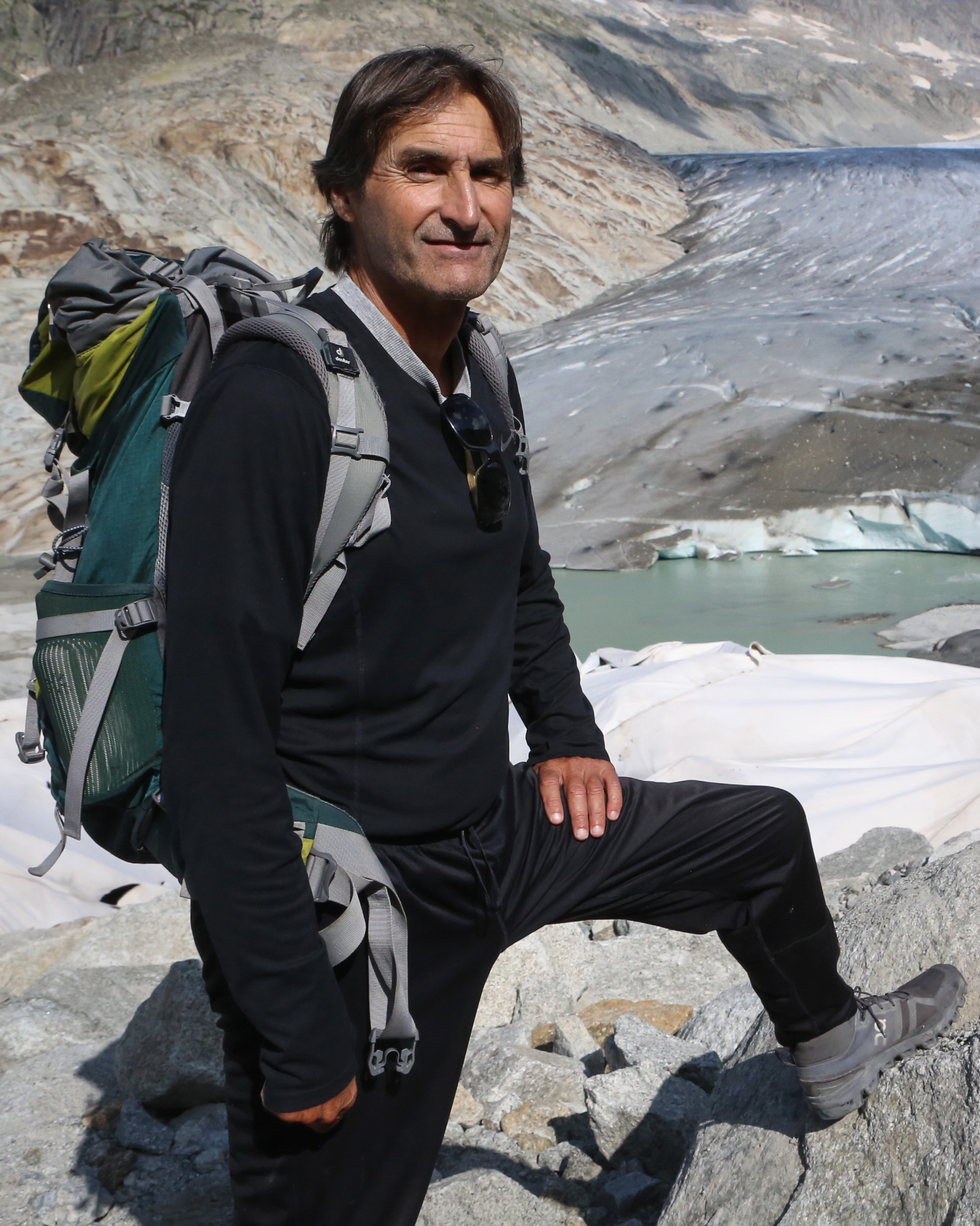 un uomo con uno zaino è in piedi tra i massi sullo sfondo di un ghiacciaio