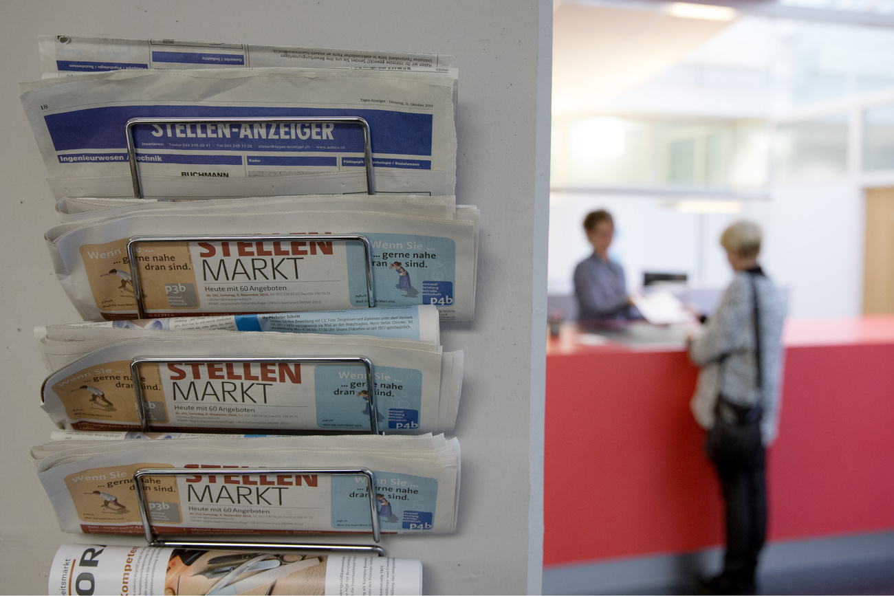 A newspaper rack with vacancies, in the foreground left, is seen in focus while a counselor of the regional employment agency RAV, left, assists an unemployed woman, right, at the counter of RAV, captured in Berne, Switzerland