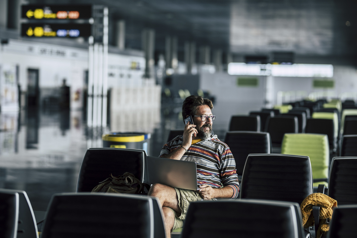 Uomo solo seduto e utilizzare il dispositivo tecnologico come il computer portatile e il telefono cellulare al gate dell'aeroporto in attesa per il suo filght
